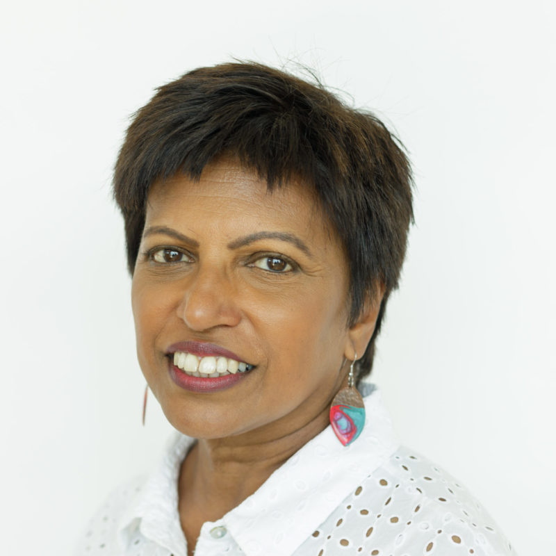 A person with warm toned light brown skin and short black hair, wearing a white top and colourful earrings