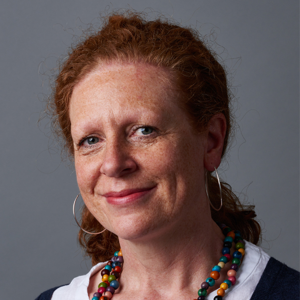 A person with a light skin tone and long auburn hair, wearing a colourful necklace and earrings